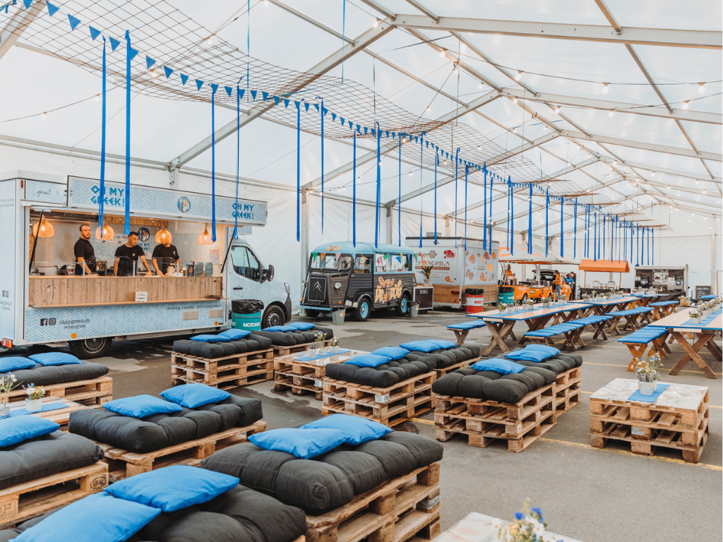 Festlich dekoriertes Zelt mit Tischen, Stehtischen, Sofas in der Firmenfarbe blau. 